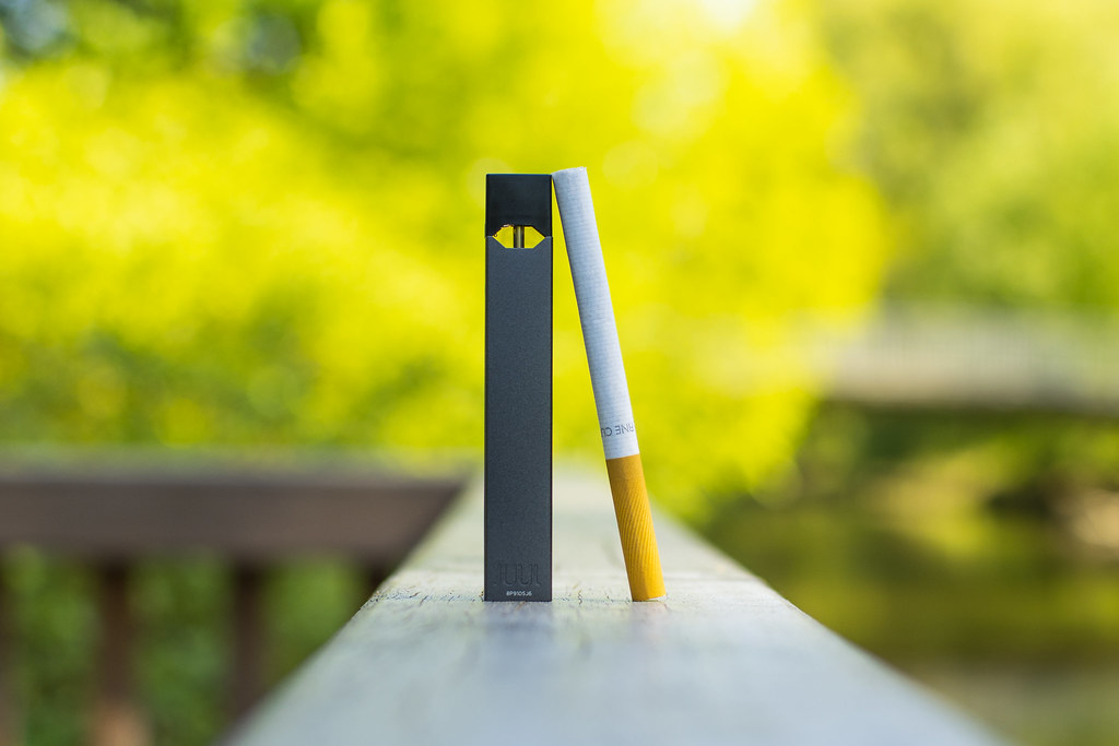 Pod vape and a cigarette standing on a railing with green blurred background